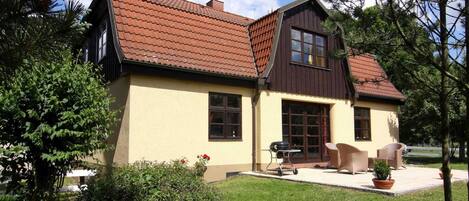 Una casa de dos pisos con techo marrón, paredes color crema y un patio con mobiliario exterior.