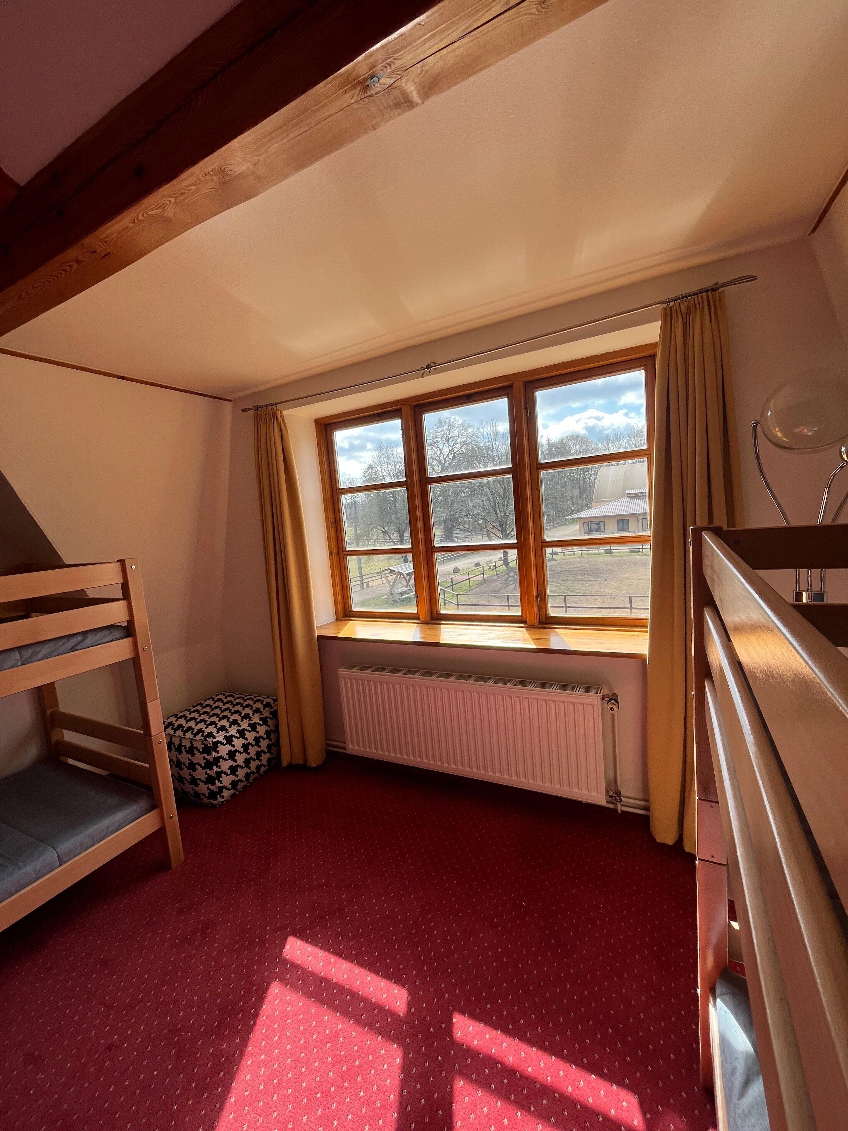 Une chambre avec un lit superposé, un radiateur, une fenêtre avec des rideaux et un bureau.