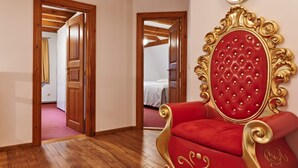 Een kamer met houten vloeren, een rode fauteuil met gouden accenten, en een spiegel aan de muur.