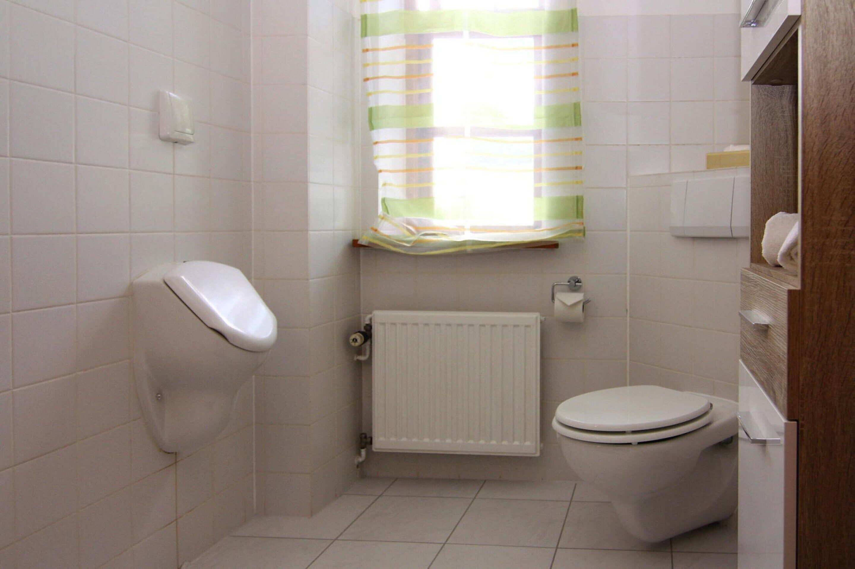 Ett litet, rent badrum med en toalett, ett element och ett fönster med en randig gardin.
