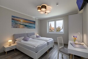 Un dormitorio moderno con dos camas, un escritorio, una silla y un ventanal con vistas a un edificio.