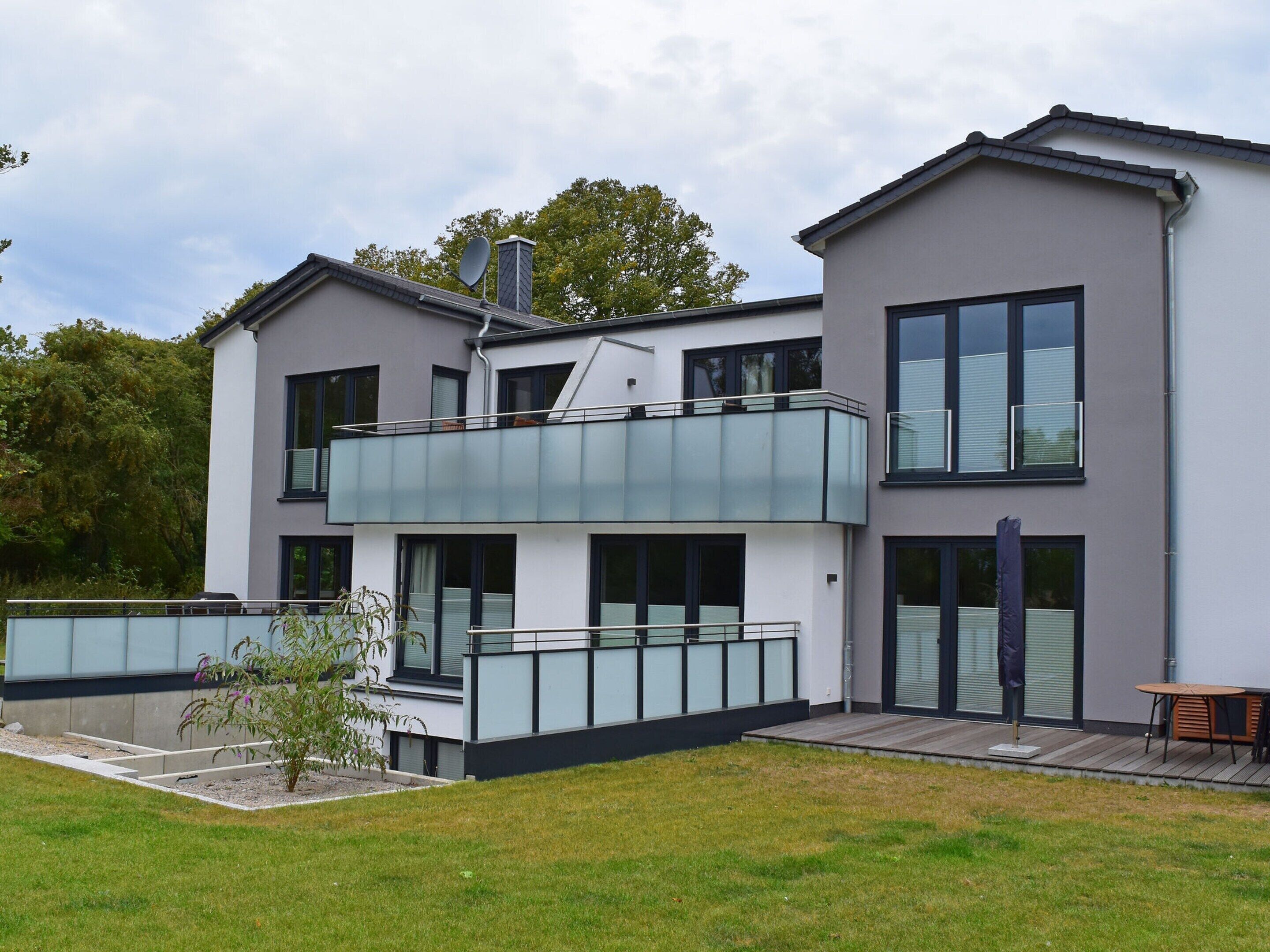 A modern two-story house with a balcony, large windows, and a small garden area.