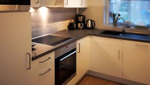 A modern kitchen with white cabinets, a built-in oven, a stovetop, and a window providing natural light. - Home Port Holiday Home, Dornum (Dornum)