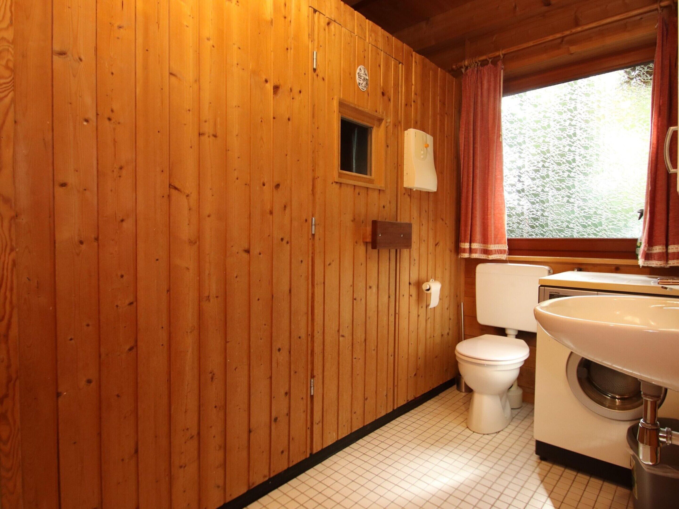 A wooden-paneled bathroom with a toilet, a sink, and a window with a curtain.