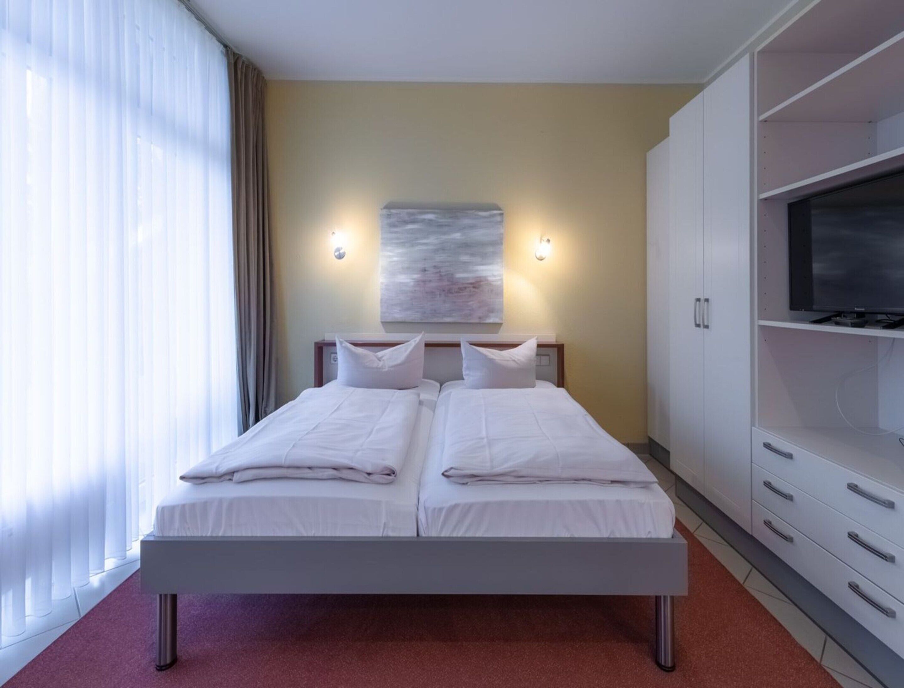 Een hotelkamer met een tweepersoonsbed, een televisie op een kastje en een schilderij aan de muur.