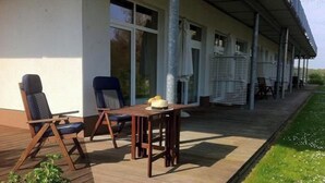 An outdoor patio with wooden furniture and a table, a covered area with chairs, and a view of the surrounding landscape. - Appartement mit Skandinavischem Flair (Mirow)