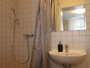 Kylpyhuone, jossa on suihku, pesuallas ja peili.