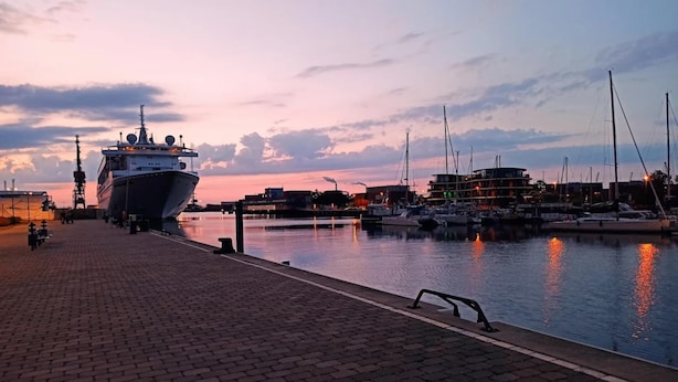 A marina with boats docked, a large ship in the foreground, and a sunset sky. - Studio in Wismar am Alten Hafen (Wismar)