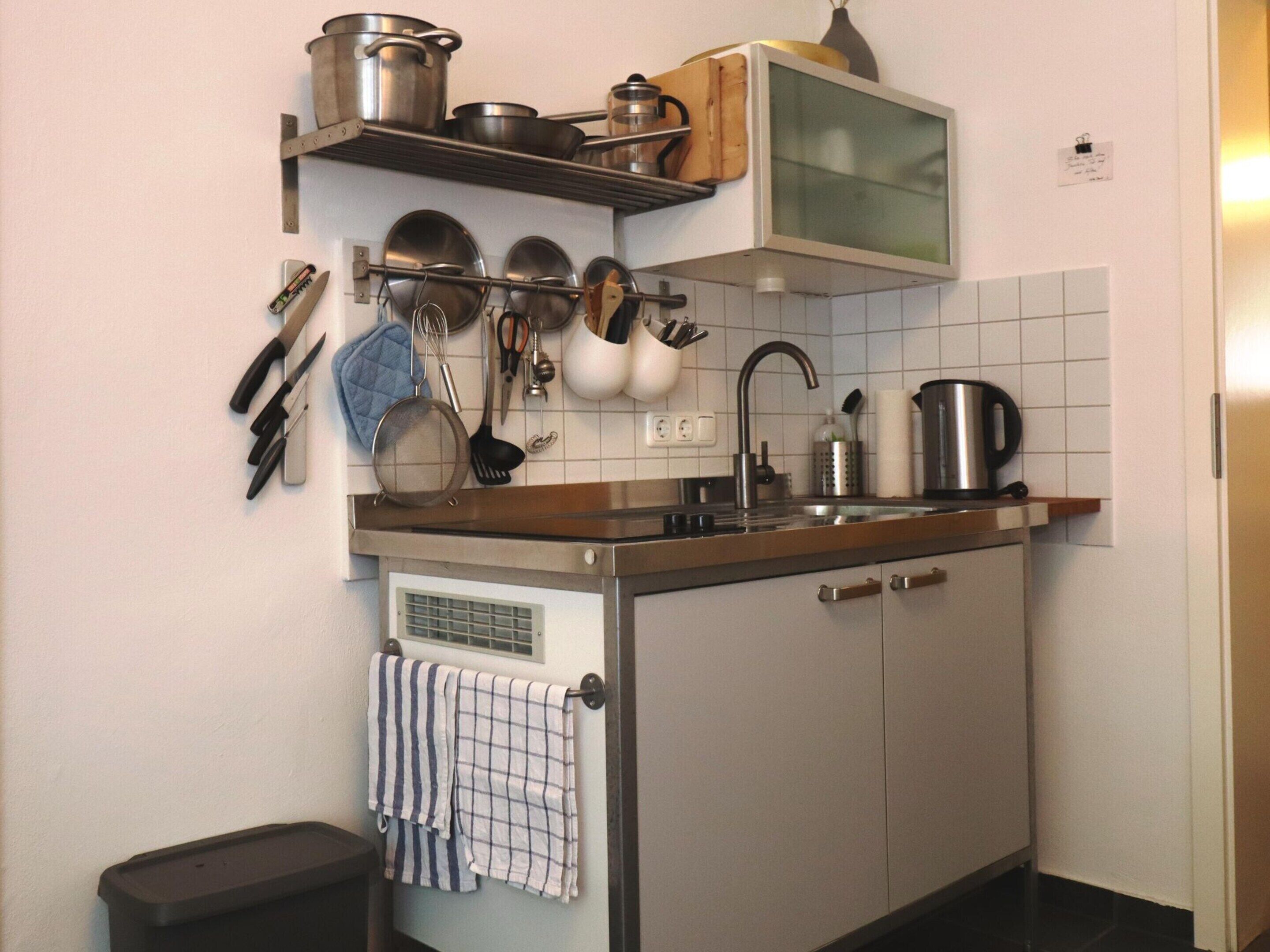 A compact kitchen with a stainless steel sink, a microwave, and various utensils hanging above the countertop.
