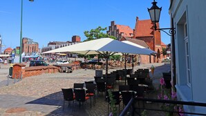 An outdoor café with tables and chairs, a cobblestone street, and historic buildings in the background. - Studio in Wismar am Alten Hafen (Wismar)