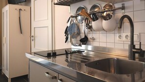 A kitchen with a stainless steel sink, a microwave, and a stove. There are pots and pans hanging on the wall, and a television mounted above the door. - Studio in Wismar am Alten Hafen (Wismar)