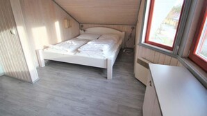 Een kleine kamer met een enkel bed, schuine wand en een raam.