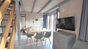 Een moderne keuken met een groot eiland, een eethoek met stoelen, een televisie op een kast en een trap.