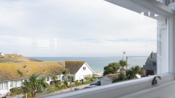 A coastal view from a window, including a white house with a tiled roof, a parked car, and a view of the sea. - Birdbank Cottage - Two Bedroom Cottage, Sleeps 4 (St Ives)