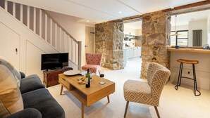 A living room with a TV, wooden coffee table, patterned chairs, and a staircase. - Birdbank Cottage - Two Bedroom Cottage, Sleeps 4 (St Ives)