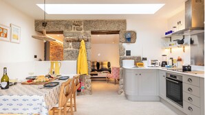 A modern kitchen with a stone archway, a dining area with a table set for two, and a cozy living space with a sofa and a coffee table. - Birdbank Cottage - Two Bedroom Cottage, Sleeps 4 (St Ives)