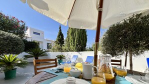 Et udendørs spiseområde med et bord dækket til morgenmad, inklusive tallerkener, bestik og en kande appelsinjuice.