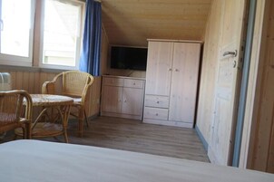 Ein Zimmer mit einem Bett, einem Esstisch mit Stühlen, einem Fernseher und Holzschränken.