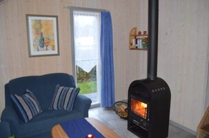 Ein gemütliches Zimmer mit einem blauen Sofa, einem Kamin und einem Fenster mit Blick ins Grüne.