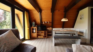 A cozy room with a wooden ceiling, a TV, a dining table, and a sofa. - Ferienhaus Amalie, Burhave (Butjadingen)