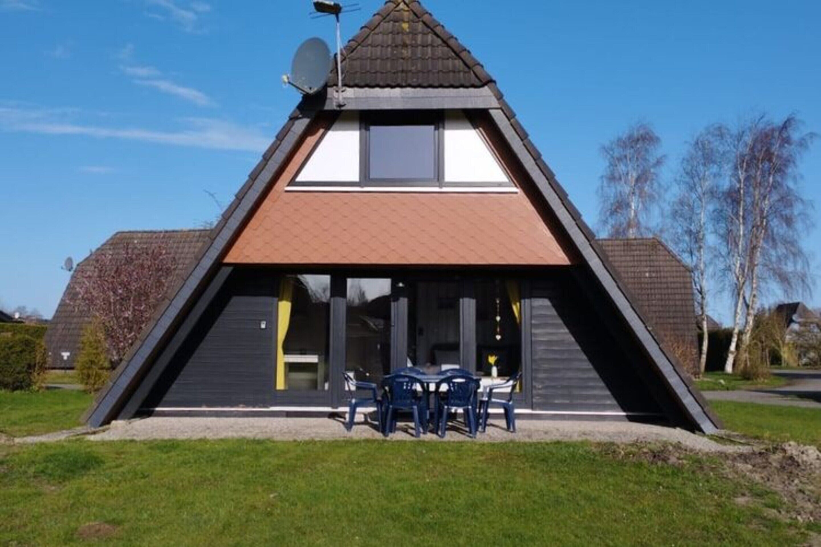 Un bâtiment de forme triangulaire, doté d’un toit plat, d’une antenne parabolique et d’une table entourée de chaises à l’avant.