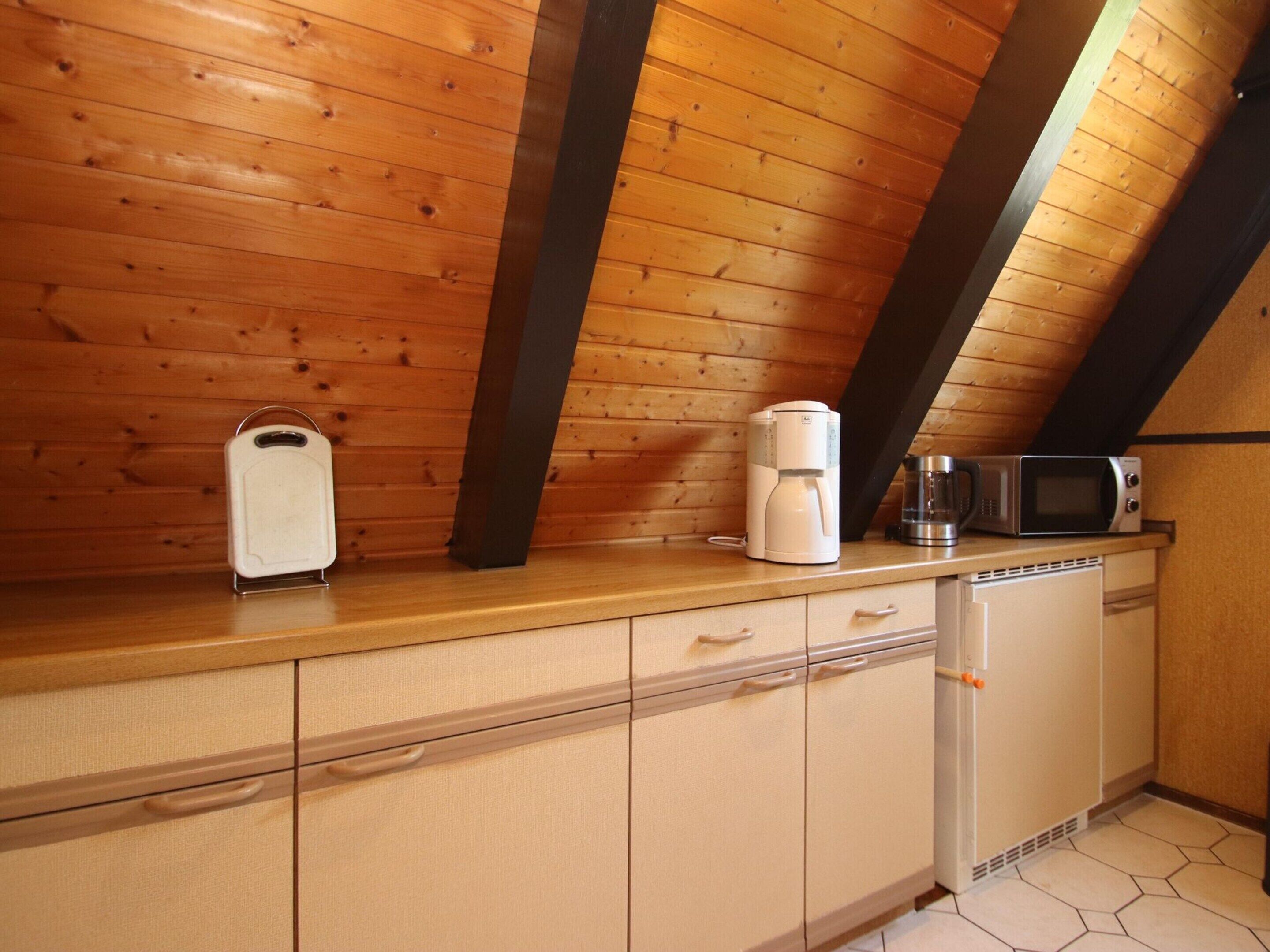 Eine Küche mit Holzwänden, einer Arbeitsplatte, einer Kaffeemaschine, einer Mikrowelle und einem Kühlschrank.