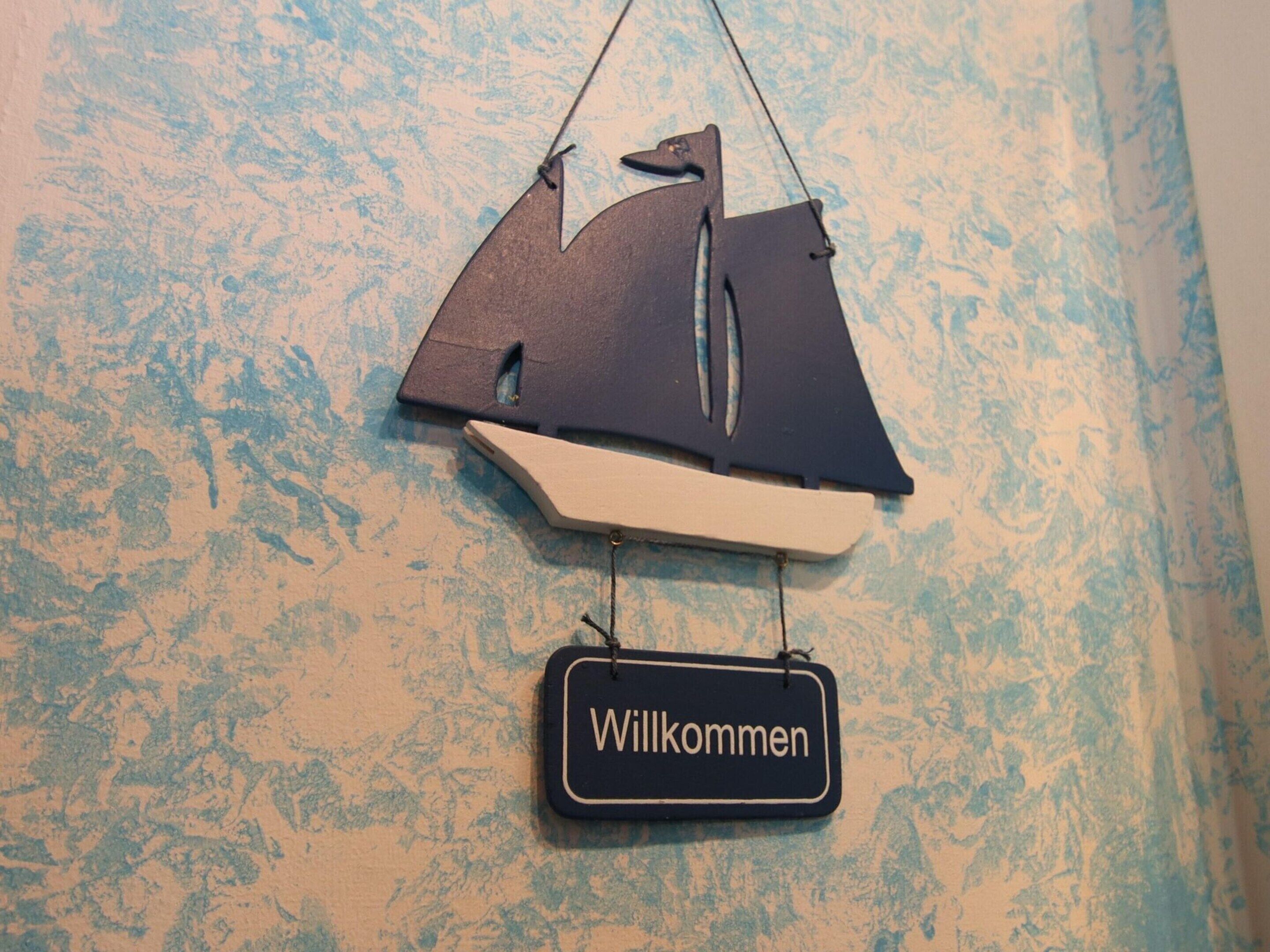 A wall-mounted decoration of a sailboat with a tag reading "Willkommen".
