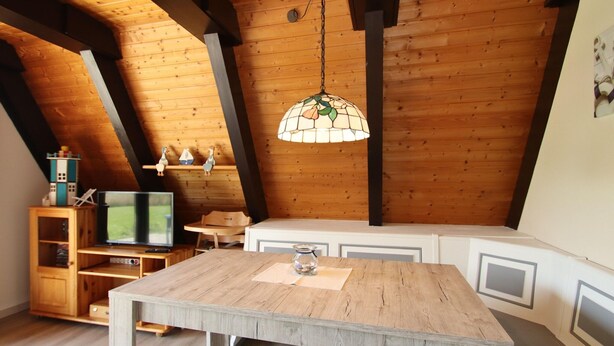 A cozy attic room with a wooden ceiling, a dining table, and a hanging lamp. - Ferienhaus Amalie, Burhave (Butjadingen)