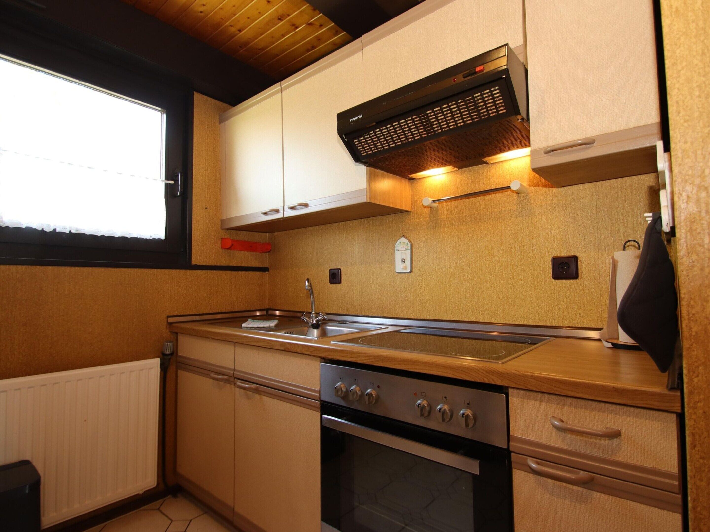 A compact kitchen with a stove, oven, sink, and a window.