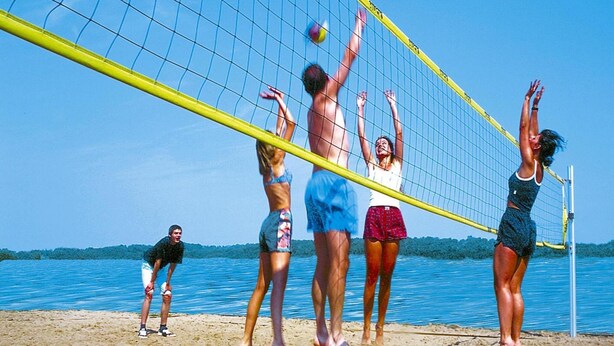 Partido de voleibol de playa con jugadores en trajes de baño.