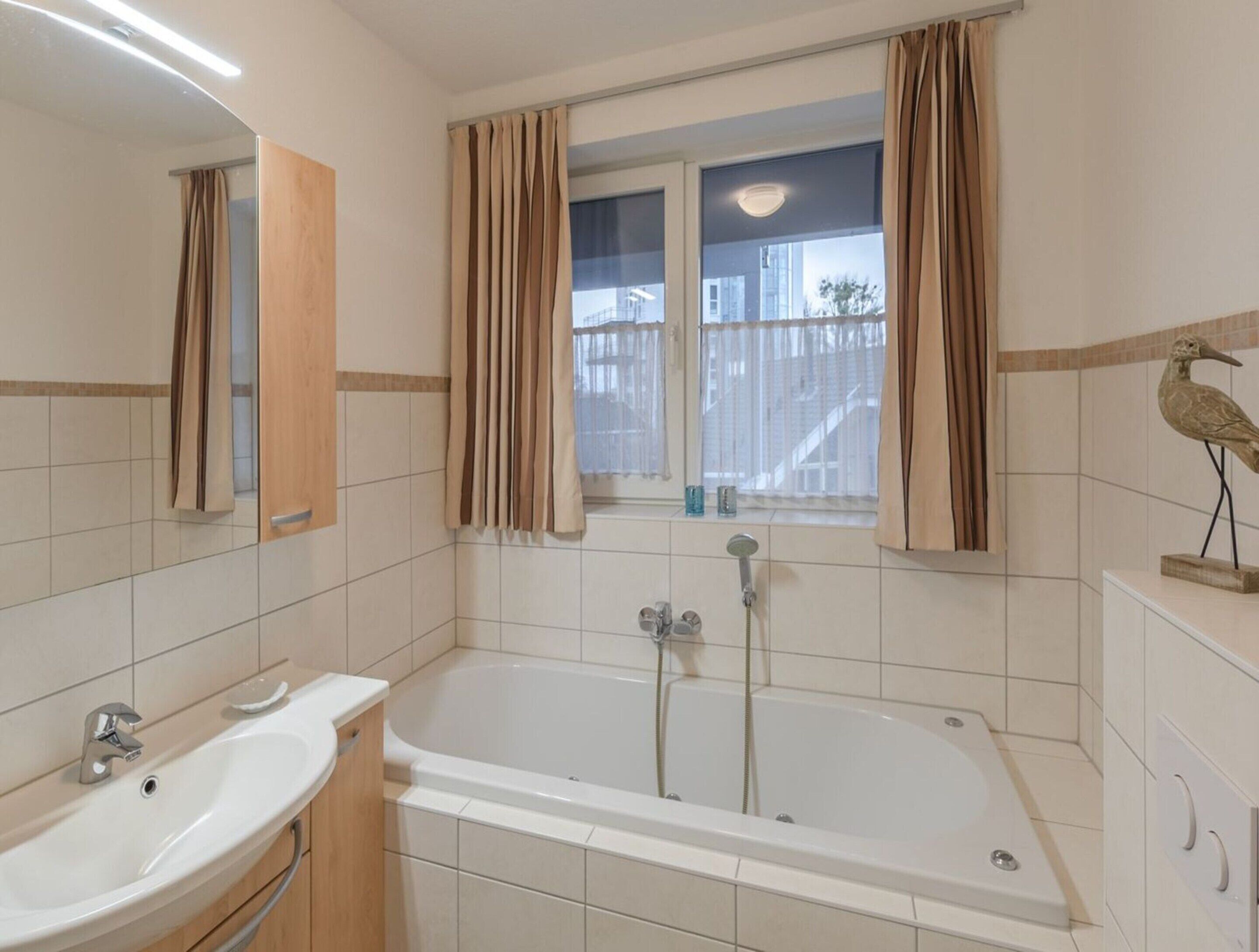 A bathroom with a bathtub, a sink, and a window with curtains.