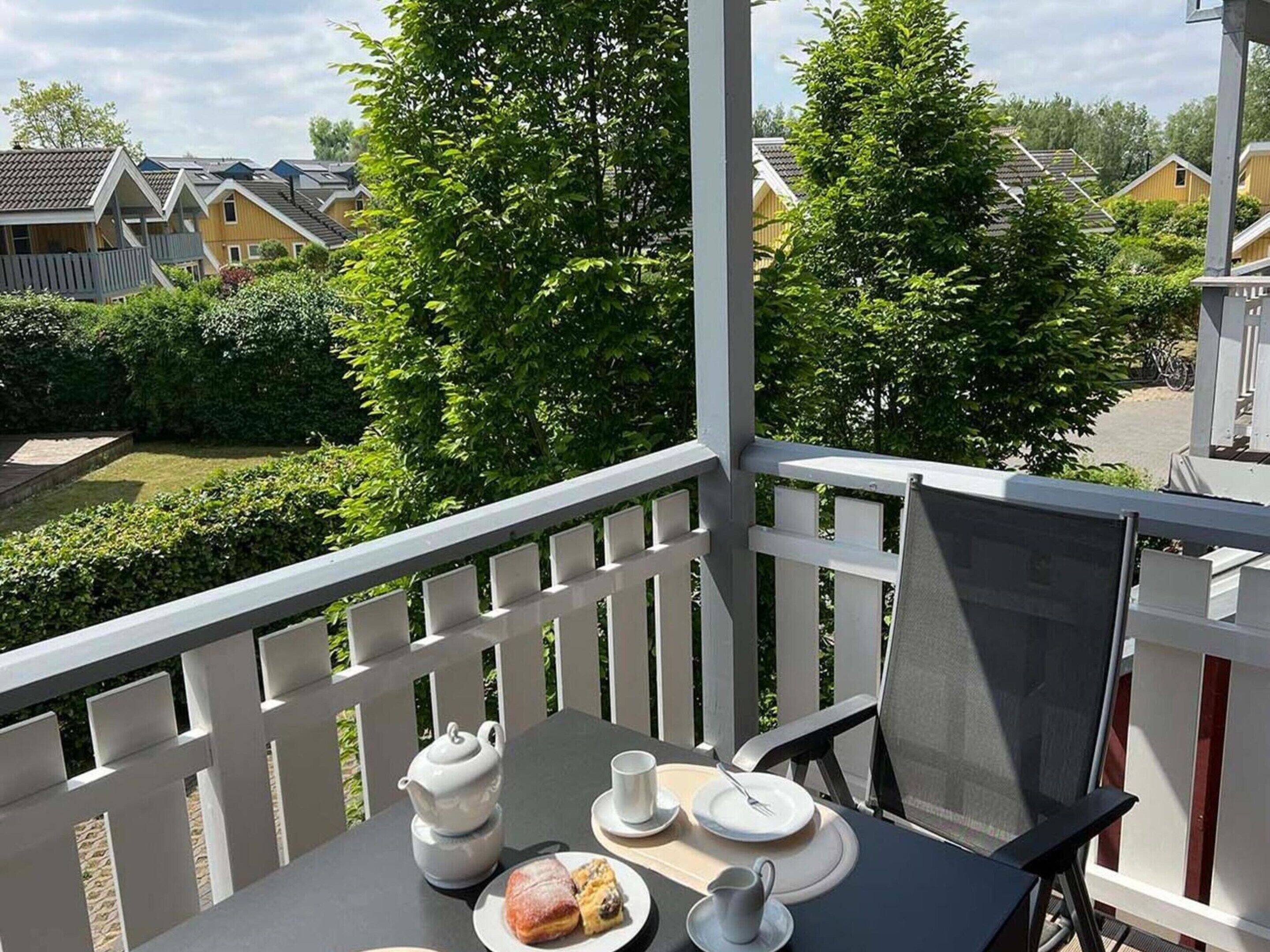 A balcony with a table set for two, a teapot, cups, and a plate of food.