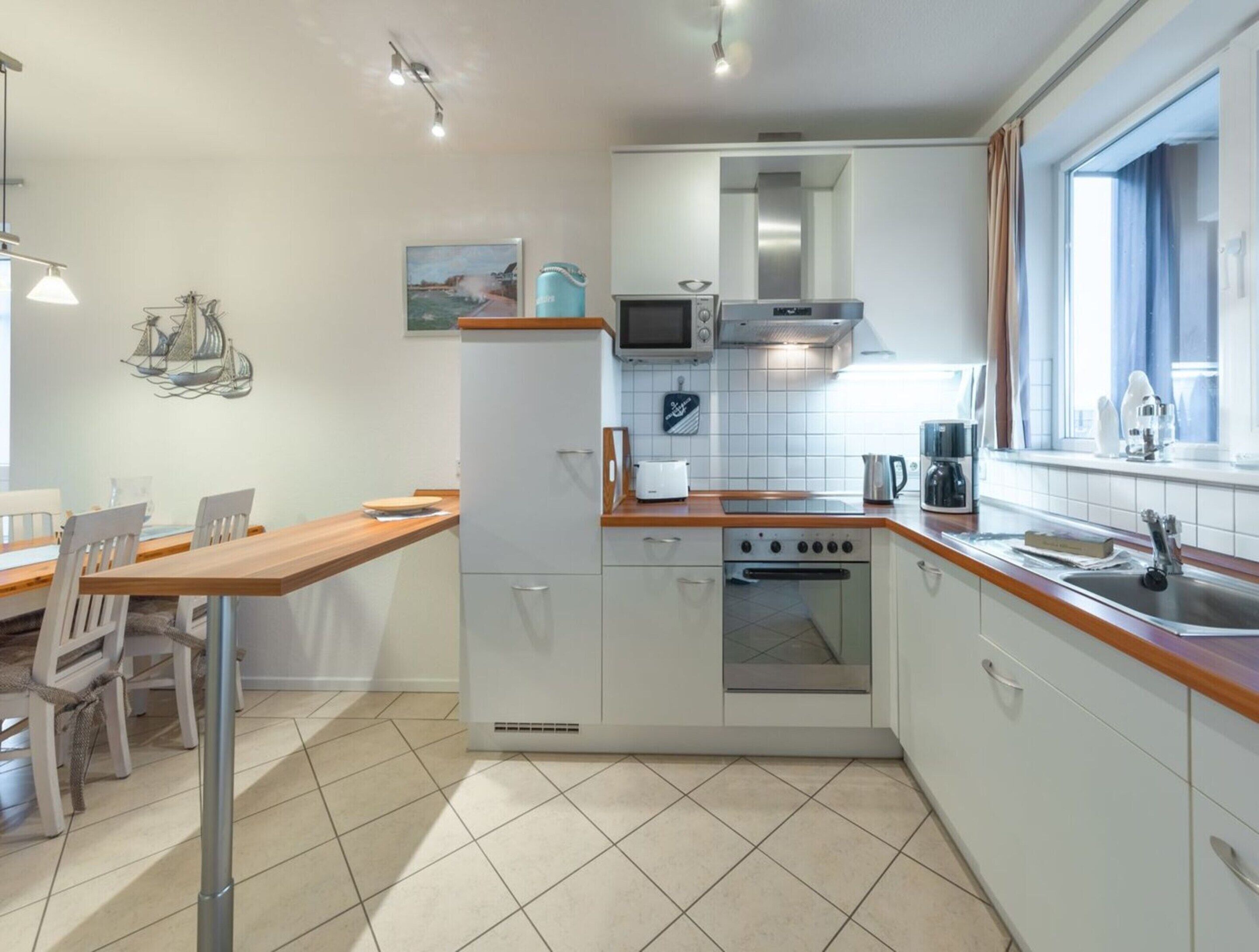 Une cuisine de taille réduite, dotée d’un plan de travail en bois, de meubles blancs, d’un four à micro-ondes, d’une cuisinière et d’un évier.