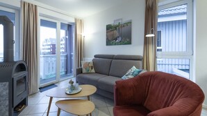 Een woonkamer met een bank, een rode fauteuil, een bijzettafeltje en een open haard.