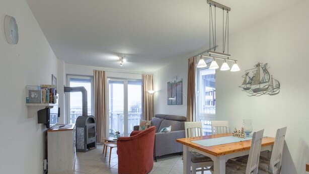 Een moderne woonkamer met een bank, een rode poef, een eettafel met stoelen en een keuken met een fornuis.