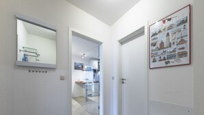Een gang met een glazen deur die leidt naar een keuken, een witte radiator en een lijst met een afbeelding aan de muur.