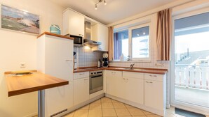Een moderne keuken met witte kasten, een houten aanrechtblad, een ingebouwde oven en een raam met gordijnen.