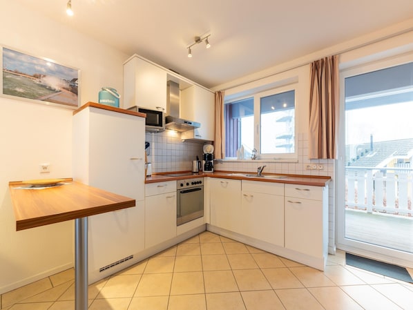 Una cucina moderna con mobili bianchi, un piano di lavoro in legno, un forno integrato e una finestra con tende.
