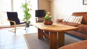 Un salon avec une table basse en bois, un fauteuil noir, un canapé marron, un téléviseur et une plante en pot.