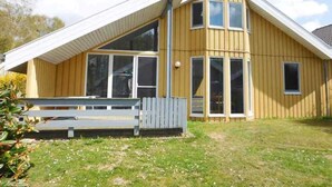 Une maison en bois à deux étages, avec un toit en pente, de grandes fenêtres et un petit porche.