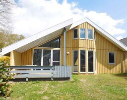 A two-story wooden house with a sloped roof, large windows, and a small porch.