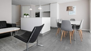 A modern kitchen with white cabinets, a dining area with a round table and grey chairs, and a black leather sofa. - 8 Person Holiday Home on a Holiday Park in Lokken (Lokken)