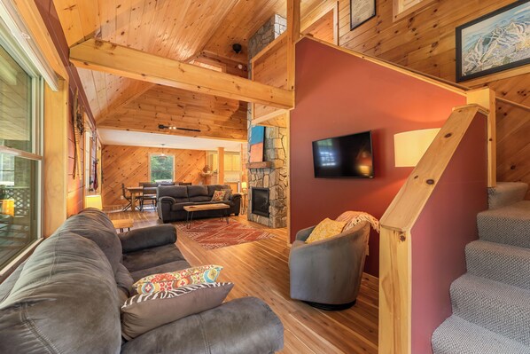 Una sala de estar acogedora con chimenea, vigas de madera y una escalera.