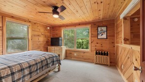 Une chambre dans un chalet en bois, avec un lit, un ventilateur de plafond, une télévision, une fenêtre et un radiateur.