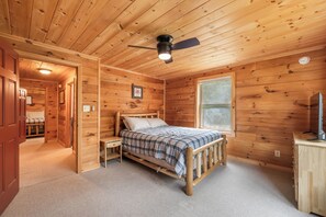 Un dormitorio de cabaña de madera con cama, mesita de noche, cómoda y ventilador de techo.