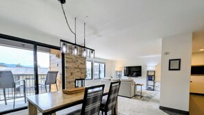Ein modernes Wohnzimmer mit Essbereich, großen Fenstern und einer Wand mit Steinverkleidung.