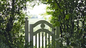 A white wooden gate with a curved top, surrounded by lush green foliage. - Angenehmes Ferienhaus fur Familien (Damp)