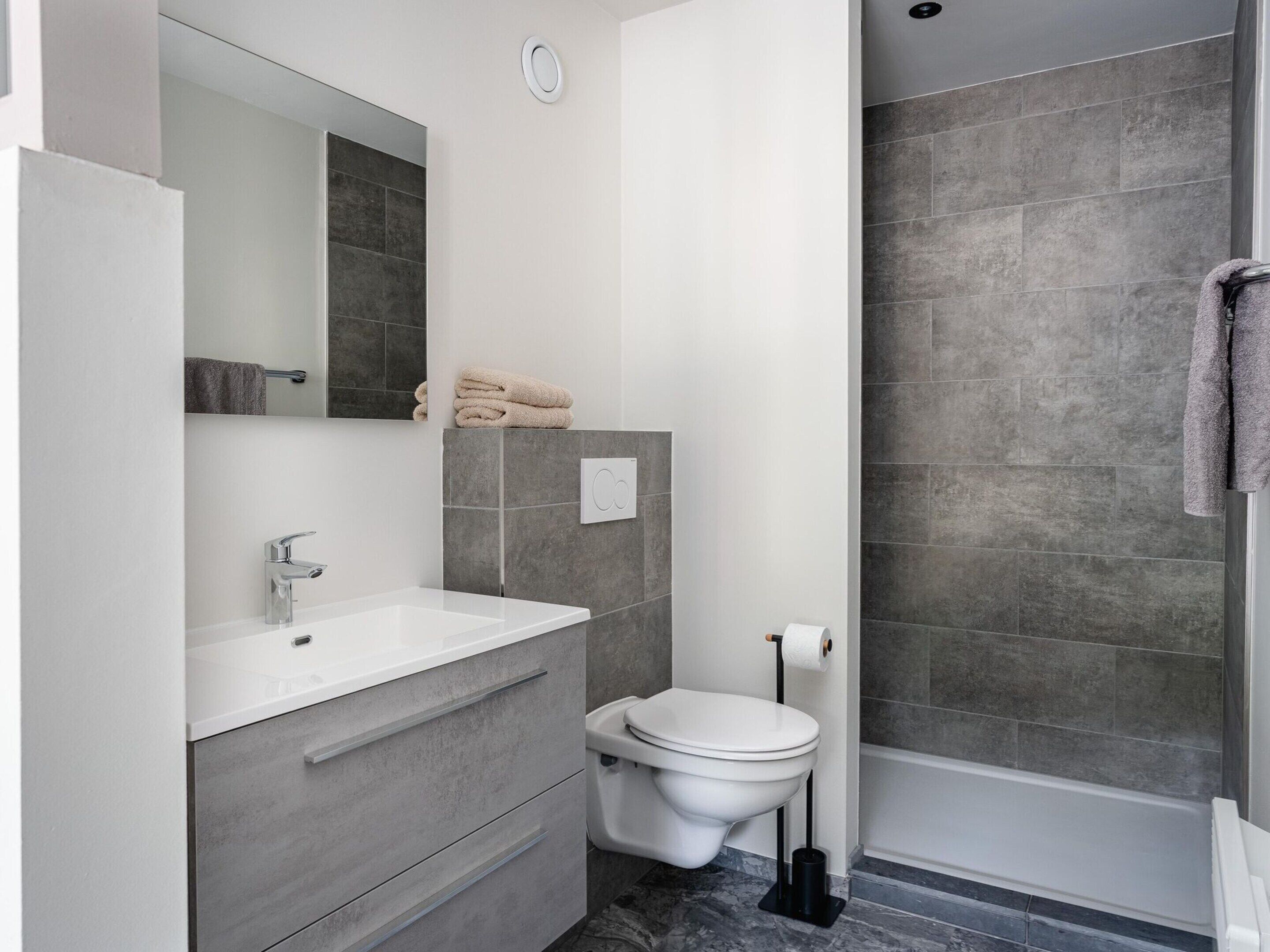 Et moderne badeværelse med en hvid vask, grå skabe, et toilet og et bruseområde.