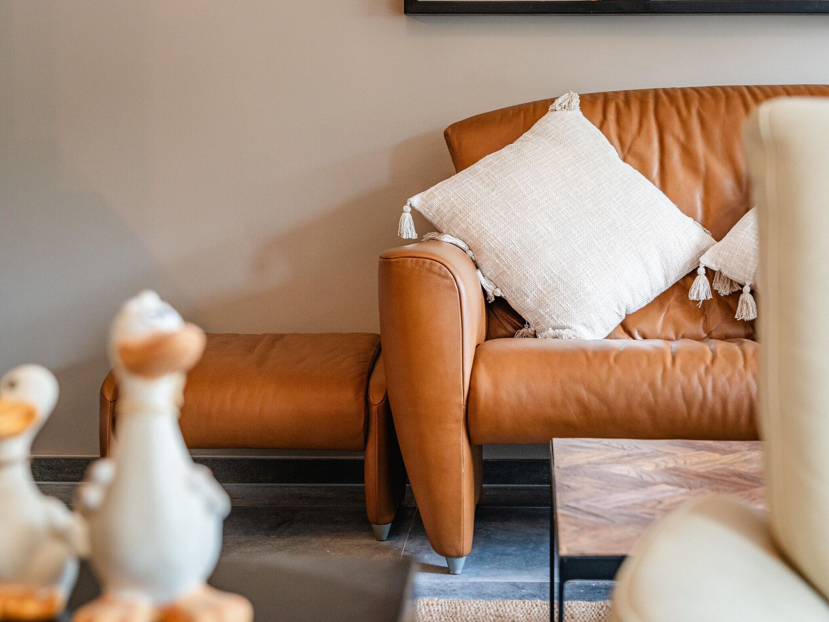 Ein beiges Ledersofa mit weißem, strukturiertem Kissen und Quasten, das an einer schlichten Wand steht.