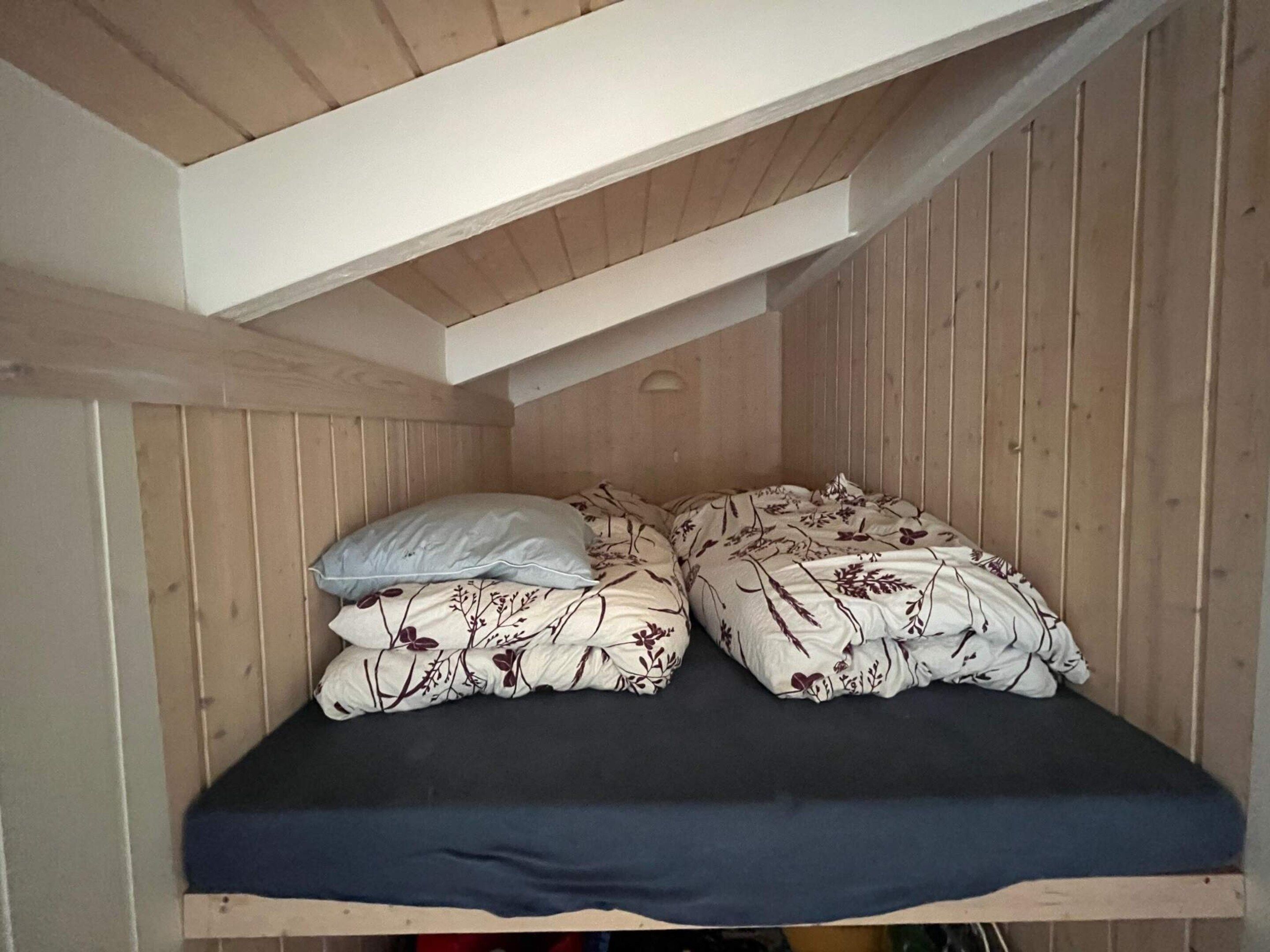 Een kleine kamer met houten lambrisering, een enkel bed met bloemenprint beddengoed en een donkerblauwe matras.